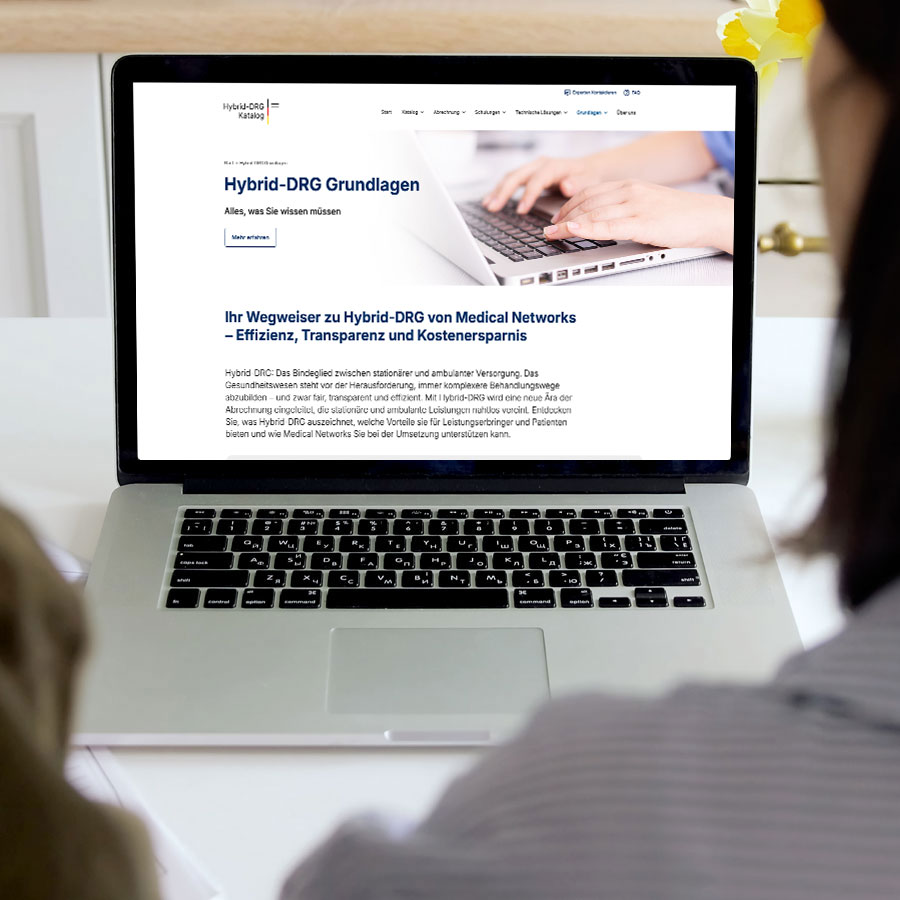 Ein Laptop im Close-Up auf dem die Website von Hybrid-DRG-Katalog.de zu sehen ist. Zwei Personen die die Seite betrachten sind angeschnitten im Vordergrund zu sehen